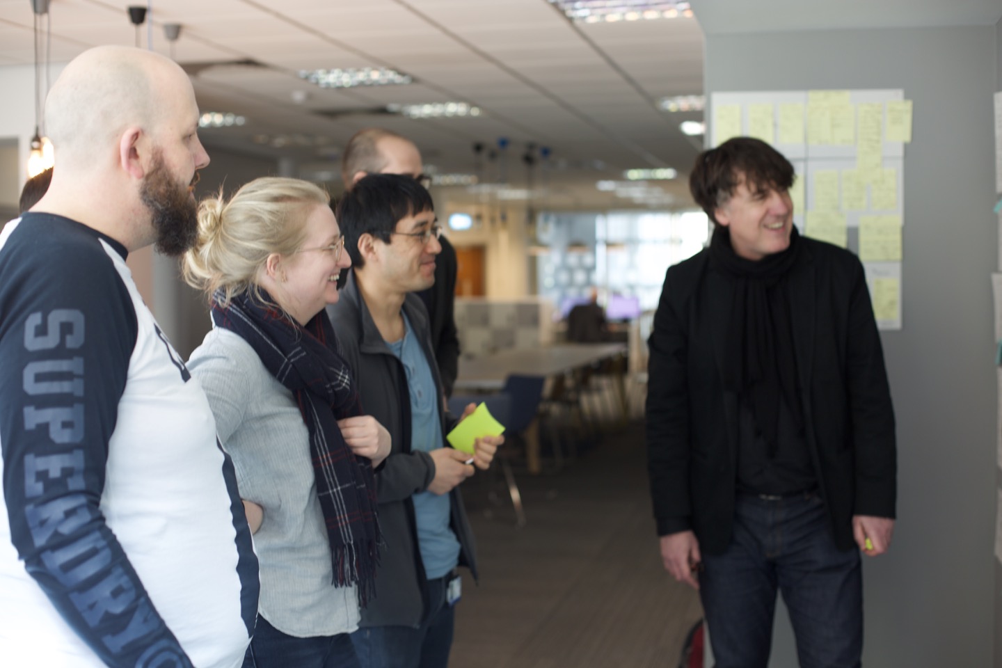 Five participants looking at the materials on a wall. They’re smiling after someone has made a joke.